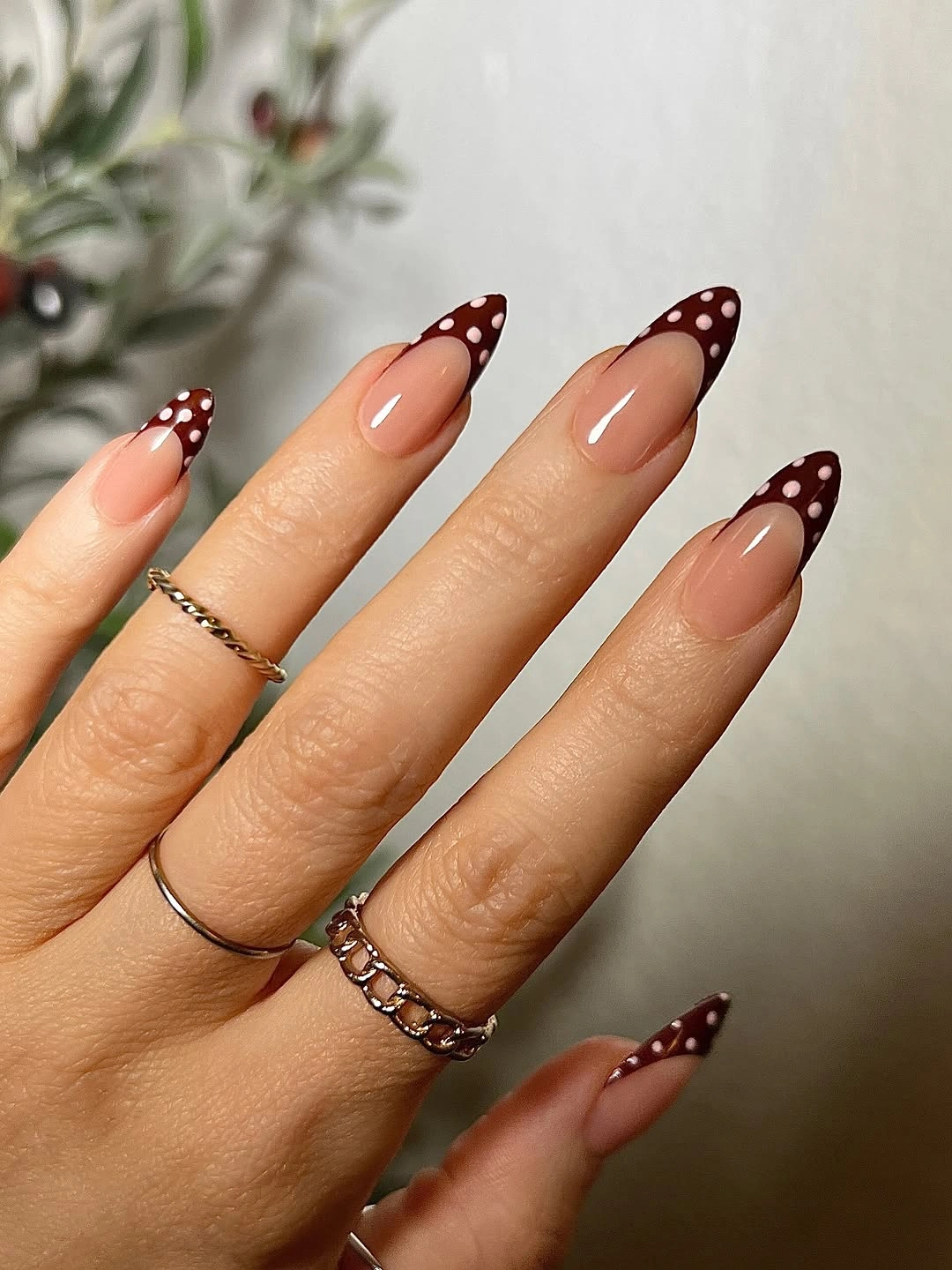 Long nude almond nails with burgundy French tips decorated by white dots