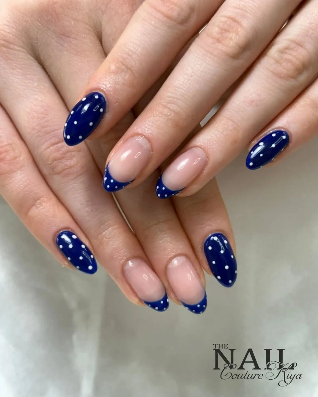 Medium nude oval nails with royal blue French edges and tiny white dots