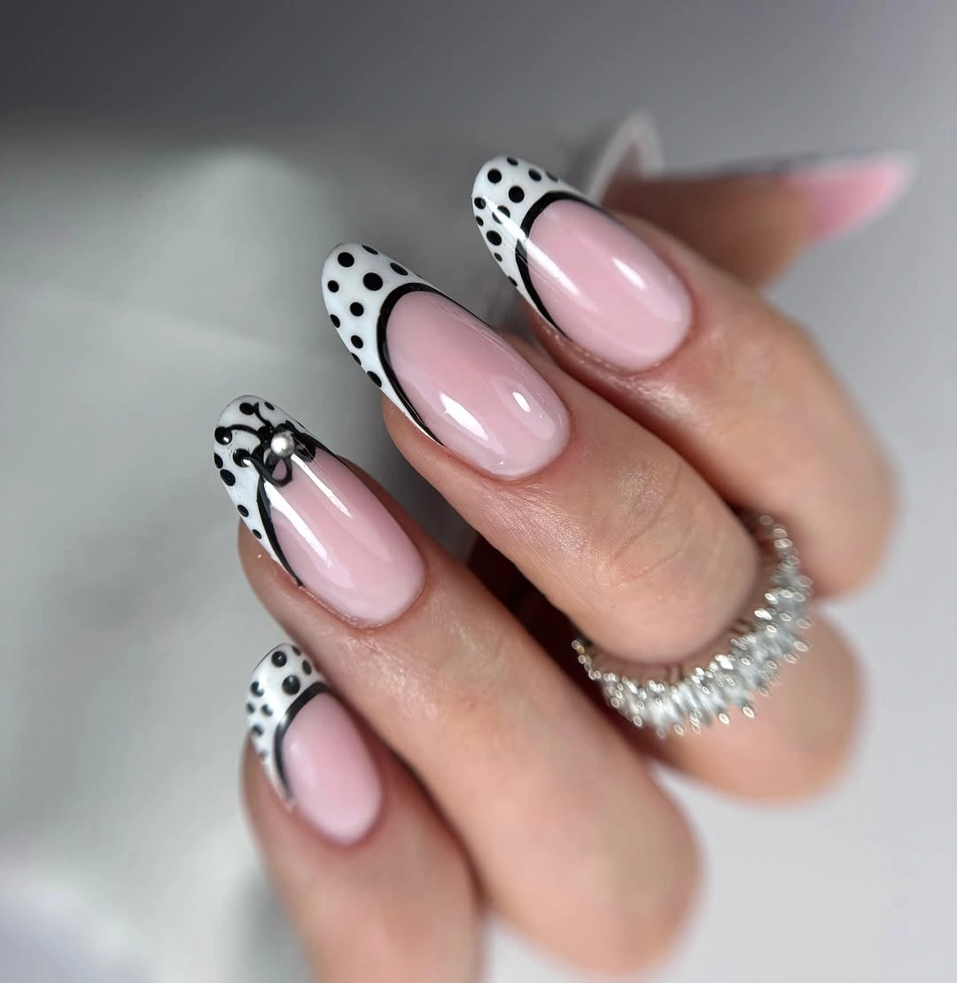 Long pale pink almond nails with white black-dotted French tips and black curve