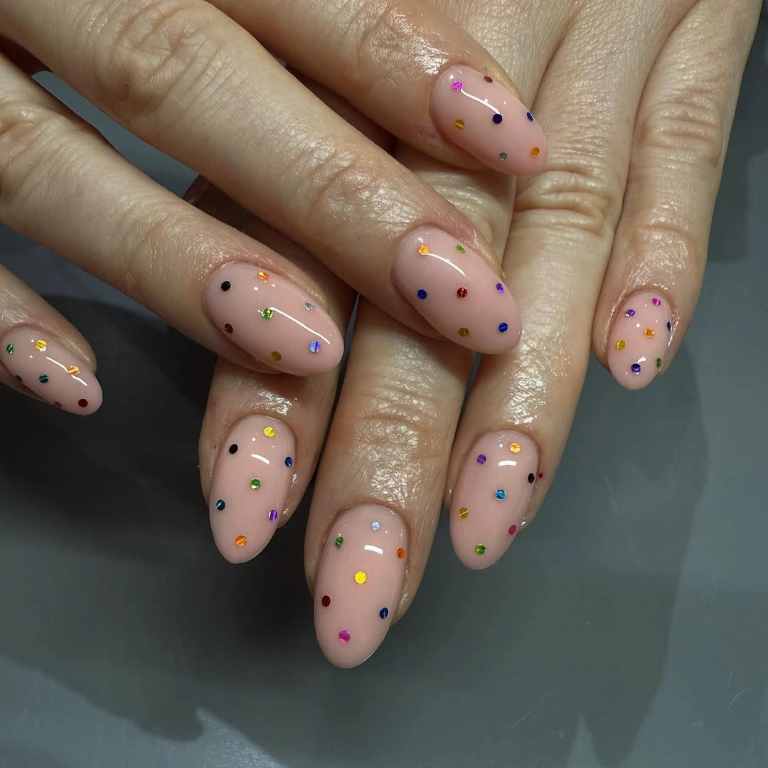 Short nude oval nails with tiny multicolor confetti dots and gold accents