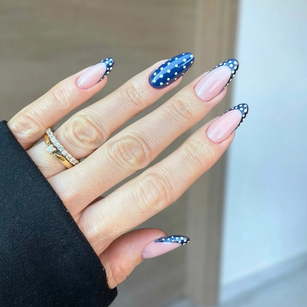 Long pale pink almond nails with navy French edges and tiny white dots