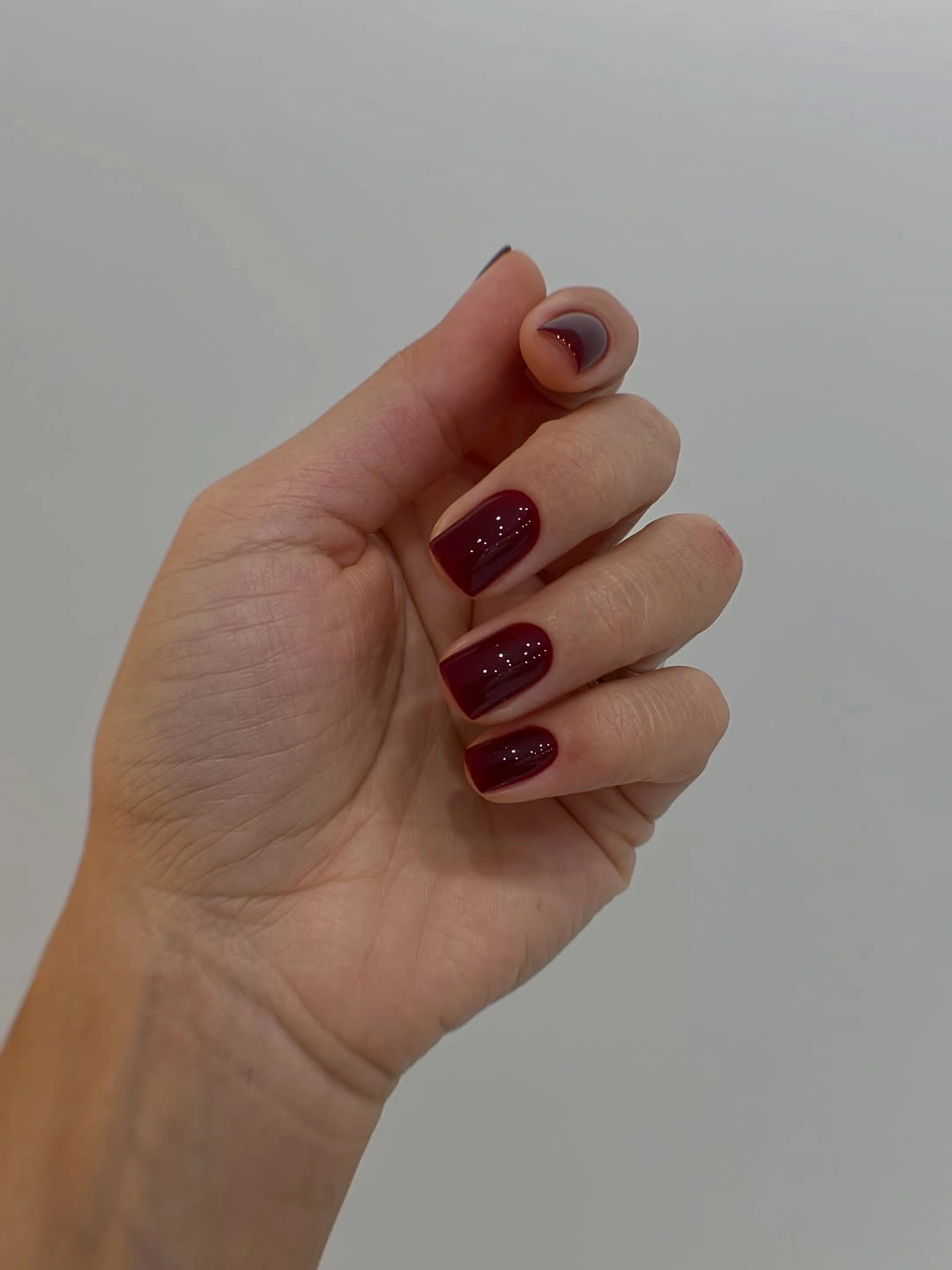Short burgundy nails with nude curved thumb accent