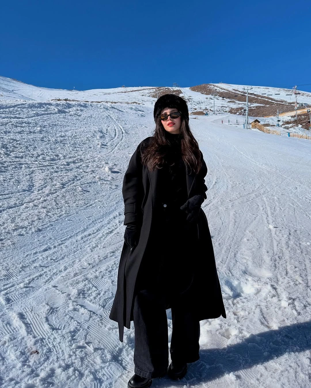 All-black long coat wide pants furry hat and sunglasses in snow