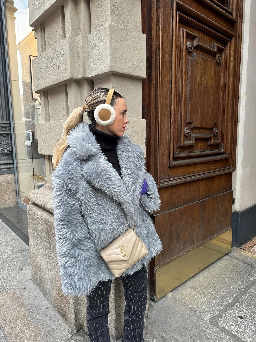 Gray textured jacket with black ribbed trousers cream earmuffs and cream bag