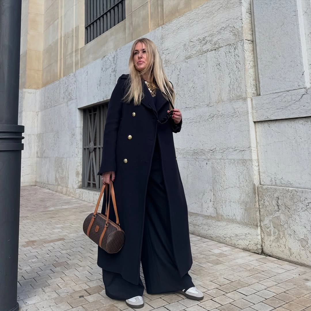 Navy double-breasted coat with dark wide trousers brown satchel and pale sneakers