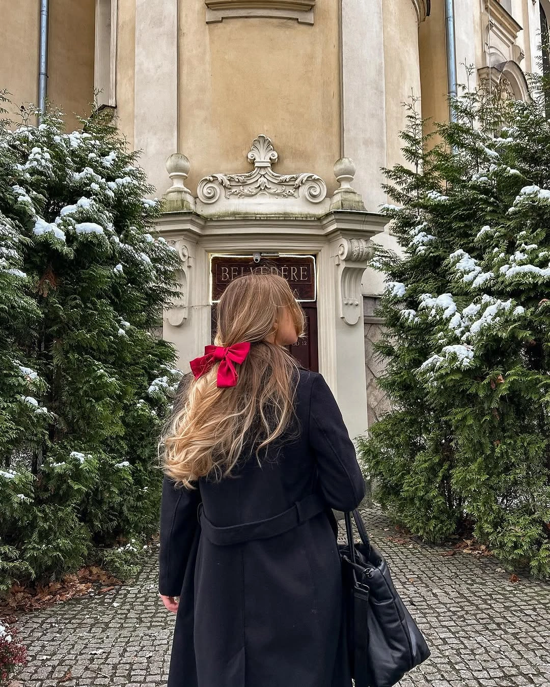 Long black coat with black tote and red hair bow