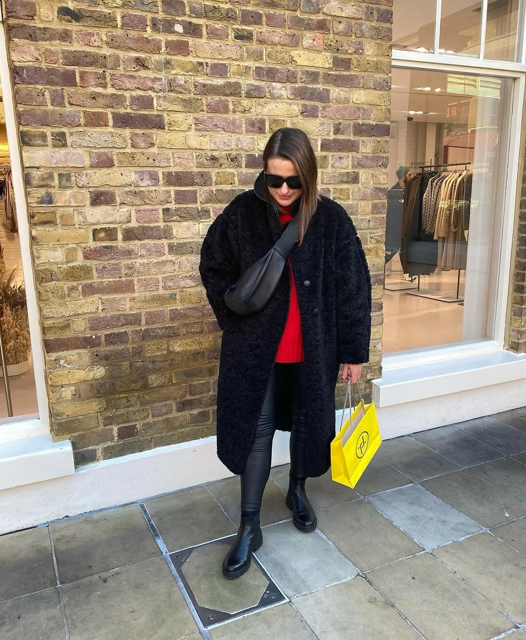 Black textured long coat with red top and yellow bag