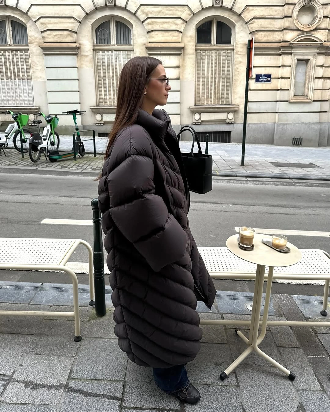 Long black puffer with black trousers, boots and handbag