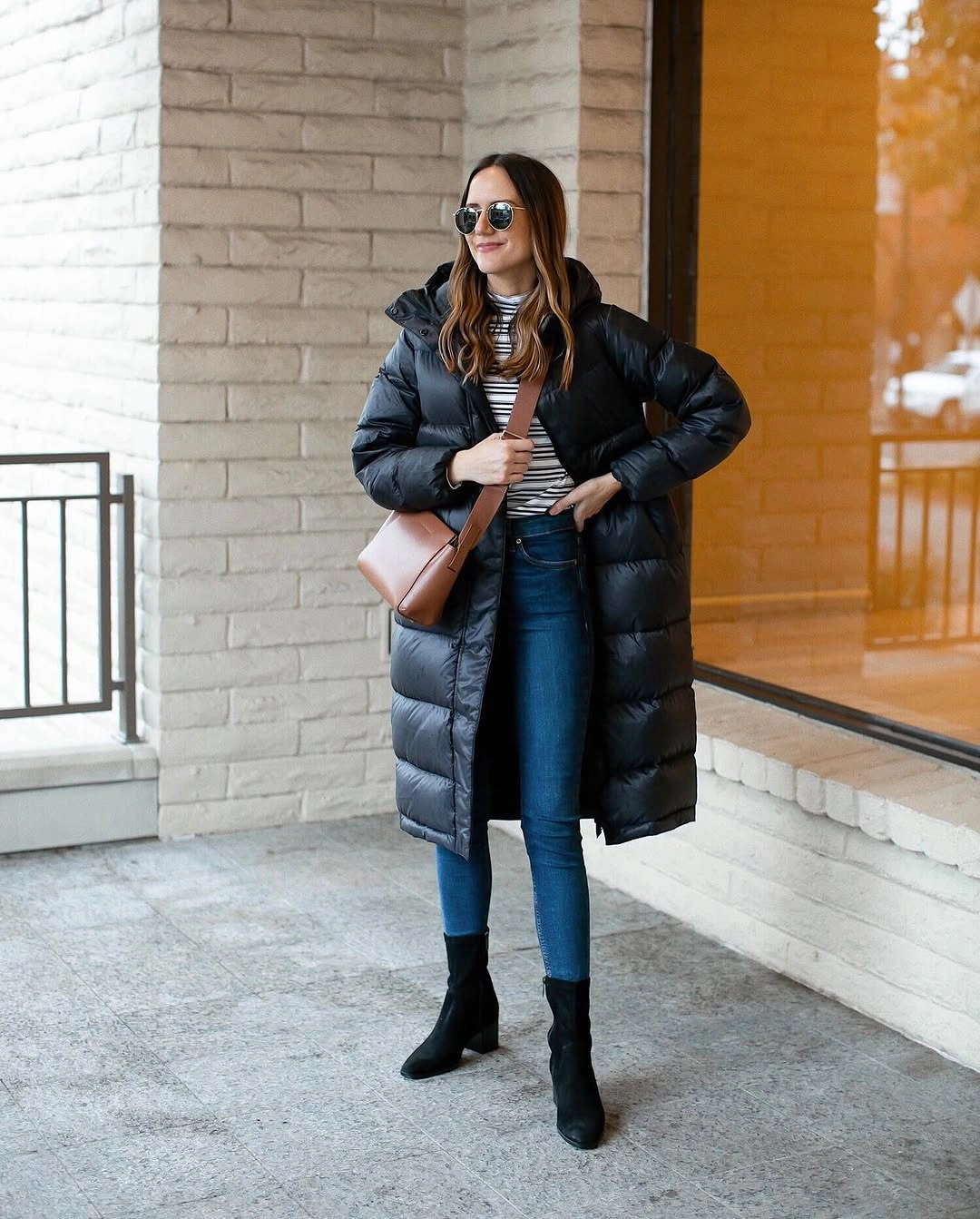 Long black puffer with striped top, jeans, boots and crossbody bag