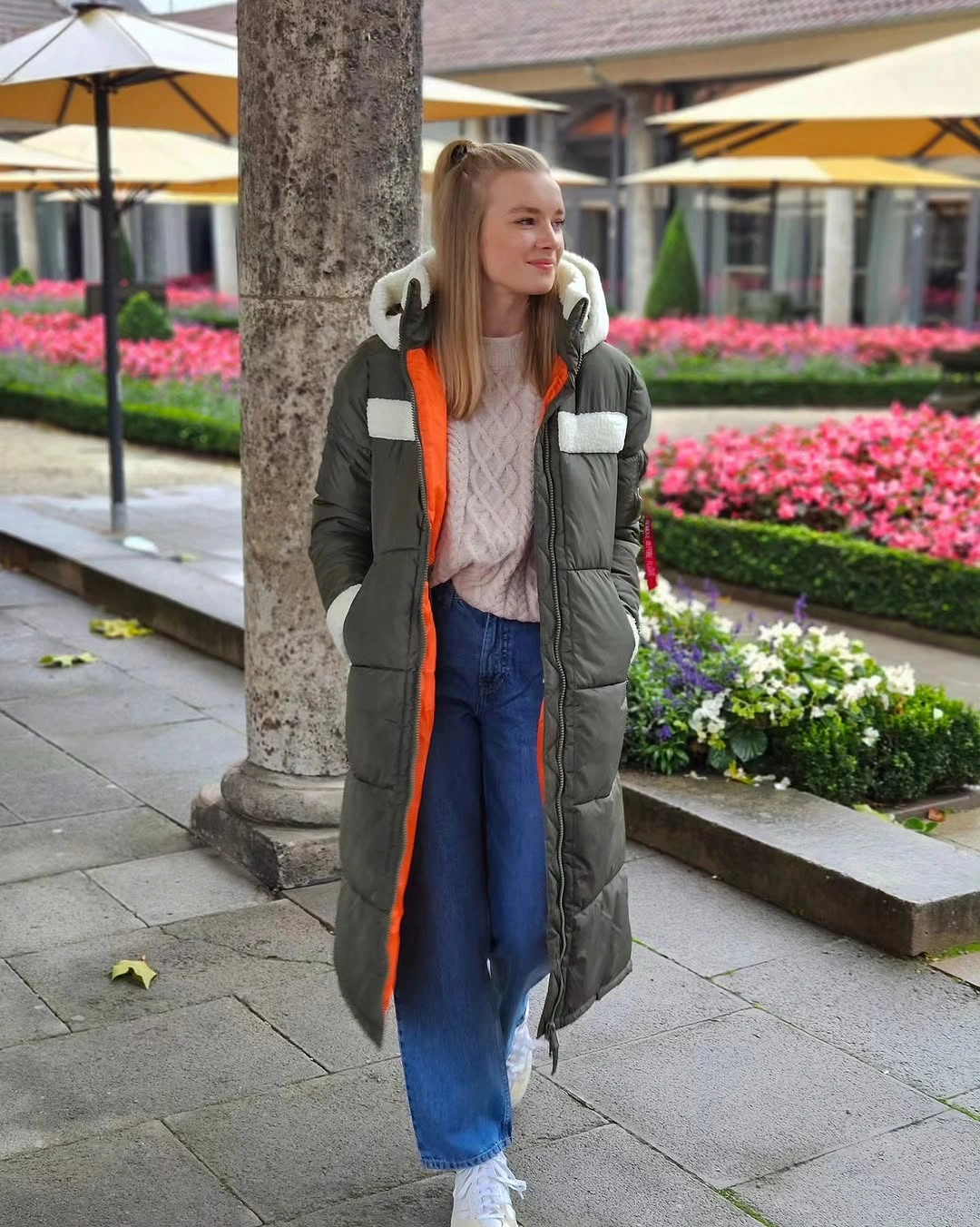 Long olive-gray puffer with orange lining, jeans and white sneakers