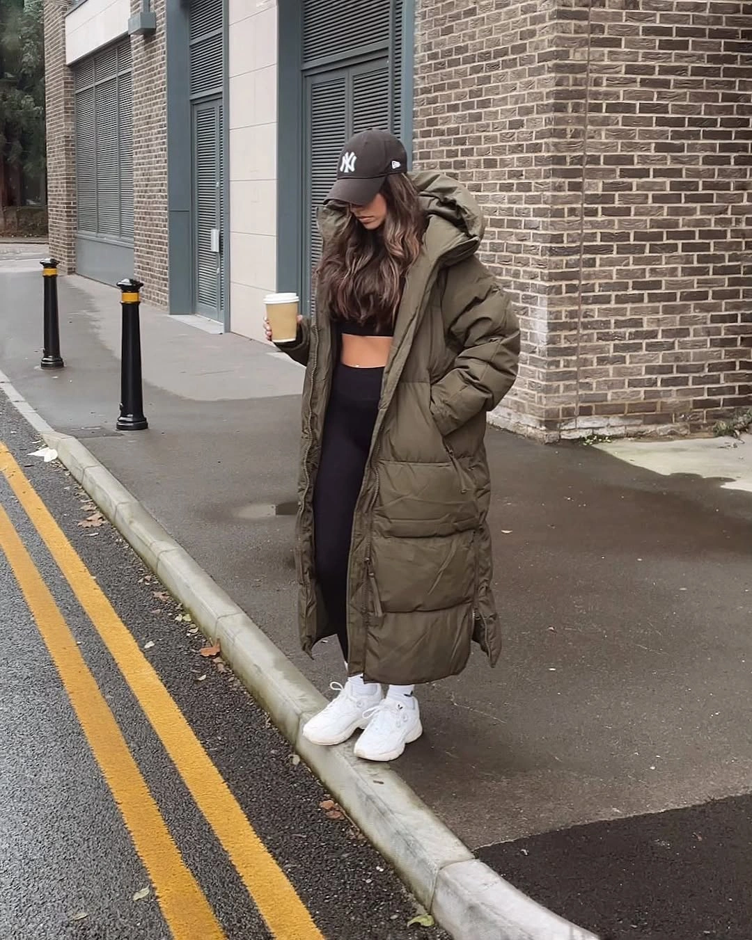 Long olive puffer worn open over dark leggings and white sneakers