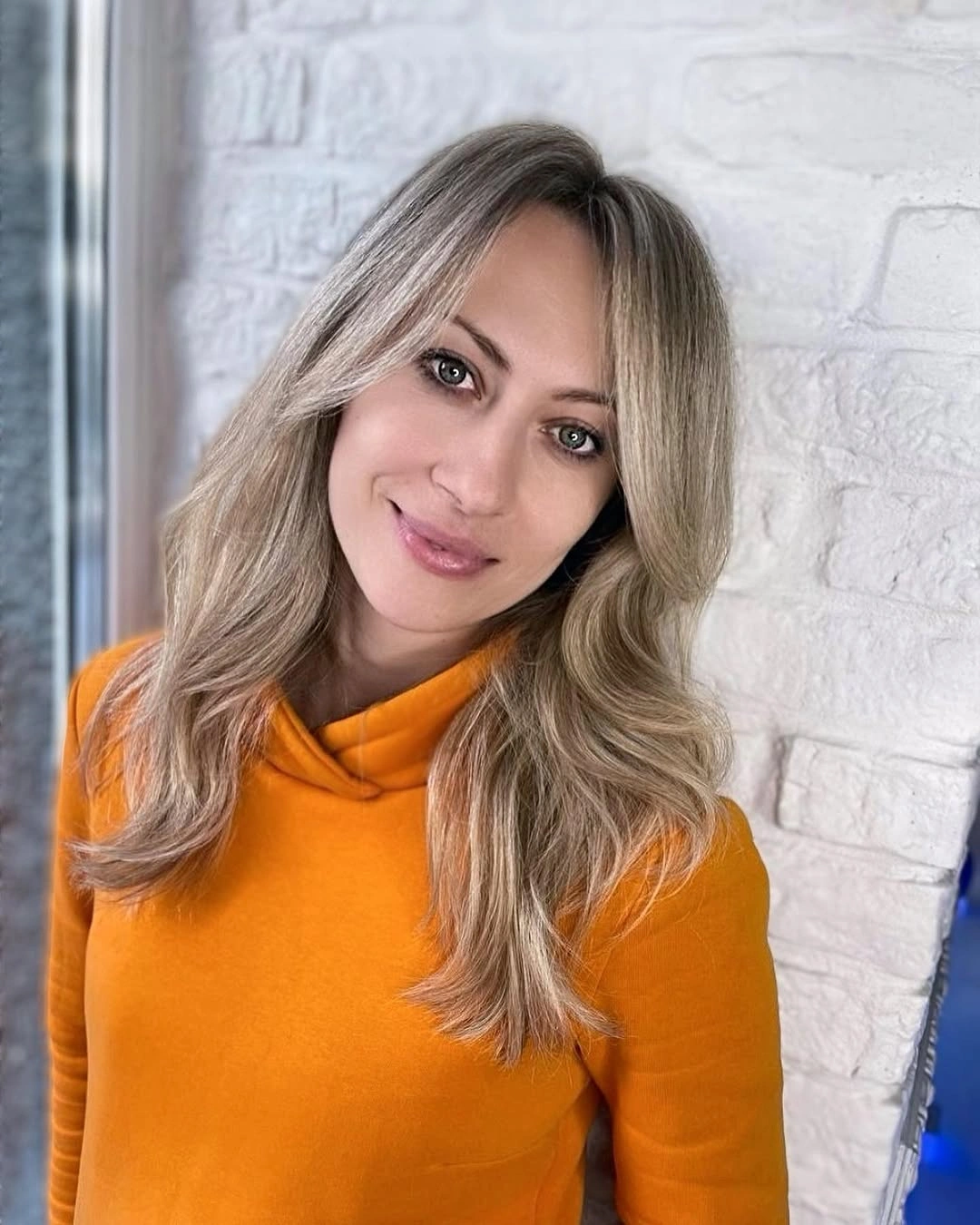 Medium-long ash blonde hair with off-center part and soft bends