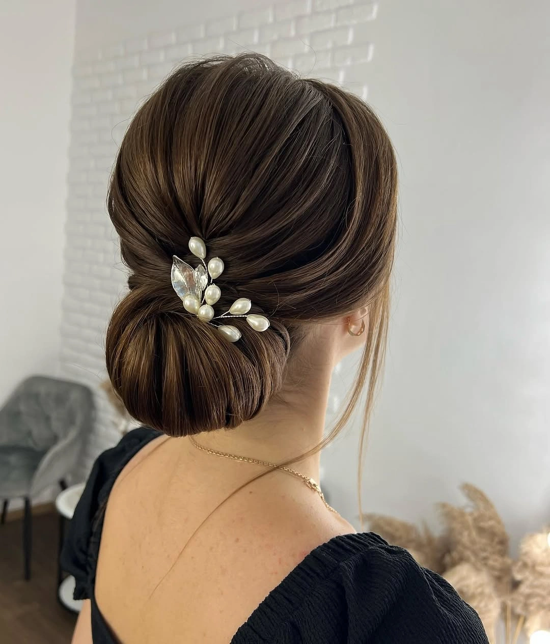 Low brunette bun with pearl-like accent above nape