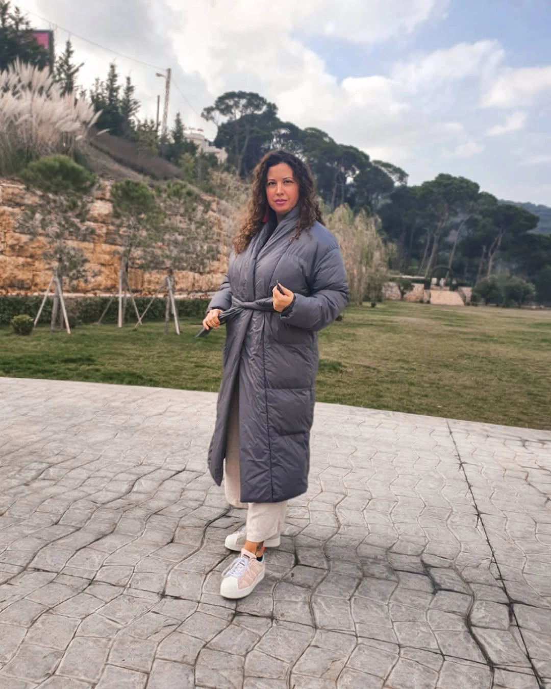 Long gray belted puffer with white trousers and sneakers