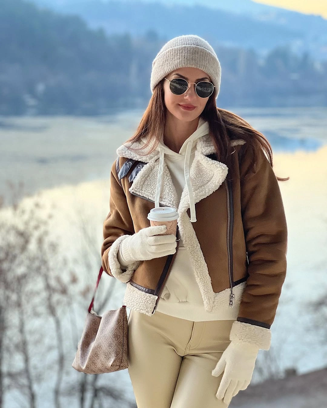 Brown trimmed aviator jacket over white hoodie and cream trousers