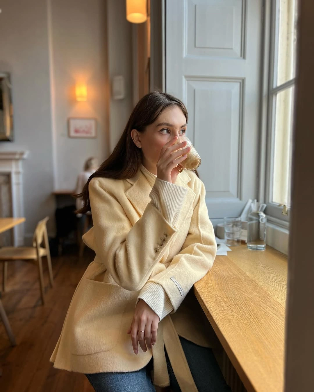 Cream coat and turtleneck styled with blue jeans indoors