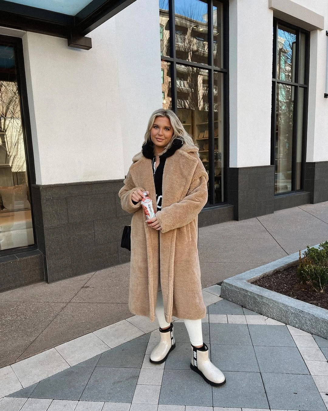 Long tan textured hooded coat with white pants and ankle boots