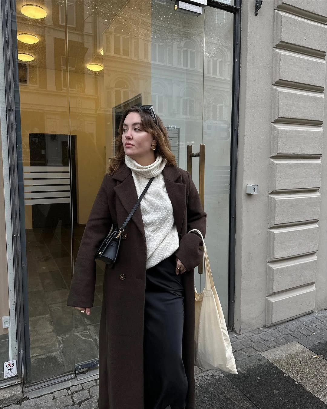 Brown double-breasted coat with ivory turtleneck and black wide trousers