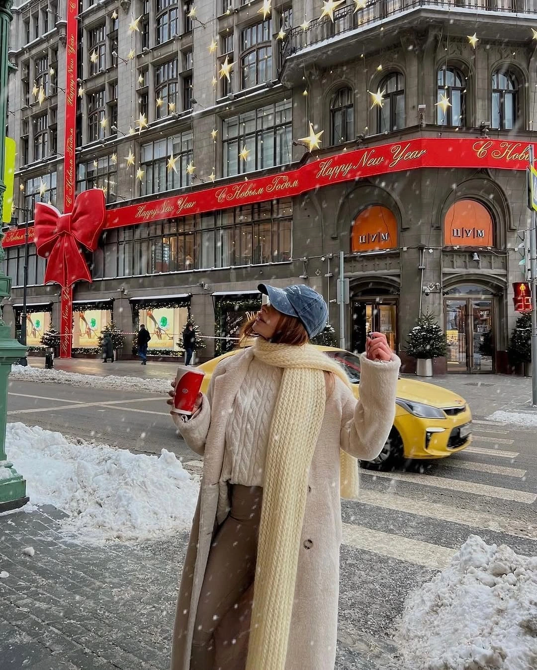 Light long coat with cream scarf, brown trousers, and dark cap