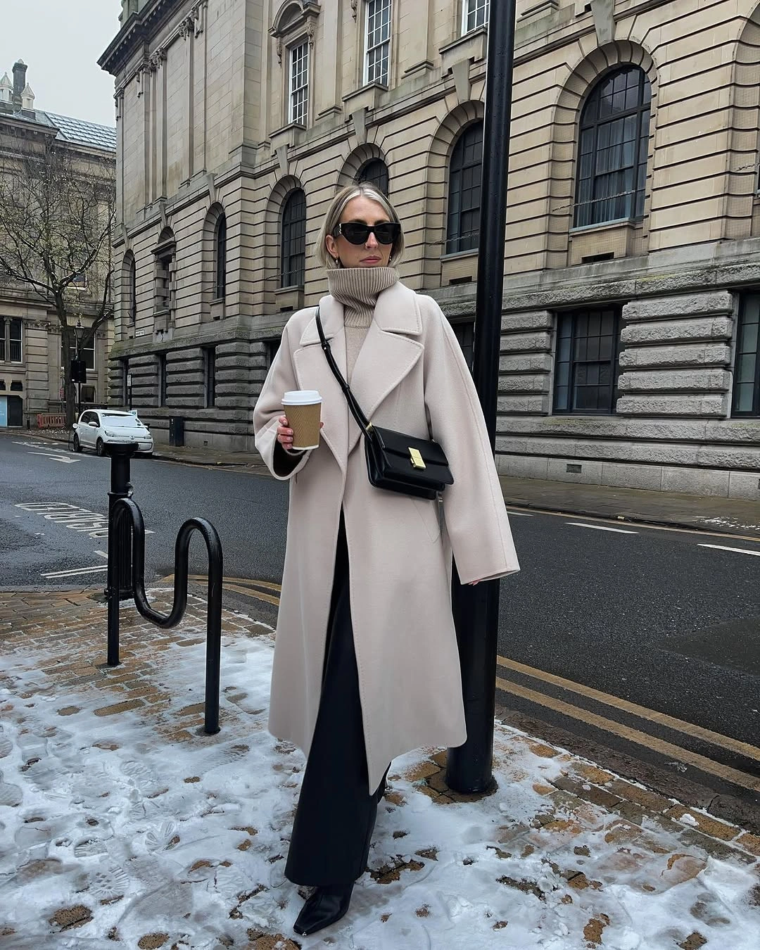 Pale long coat, taupe turtleneck, black wide trousers, and ankle boots