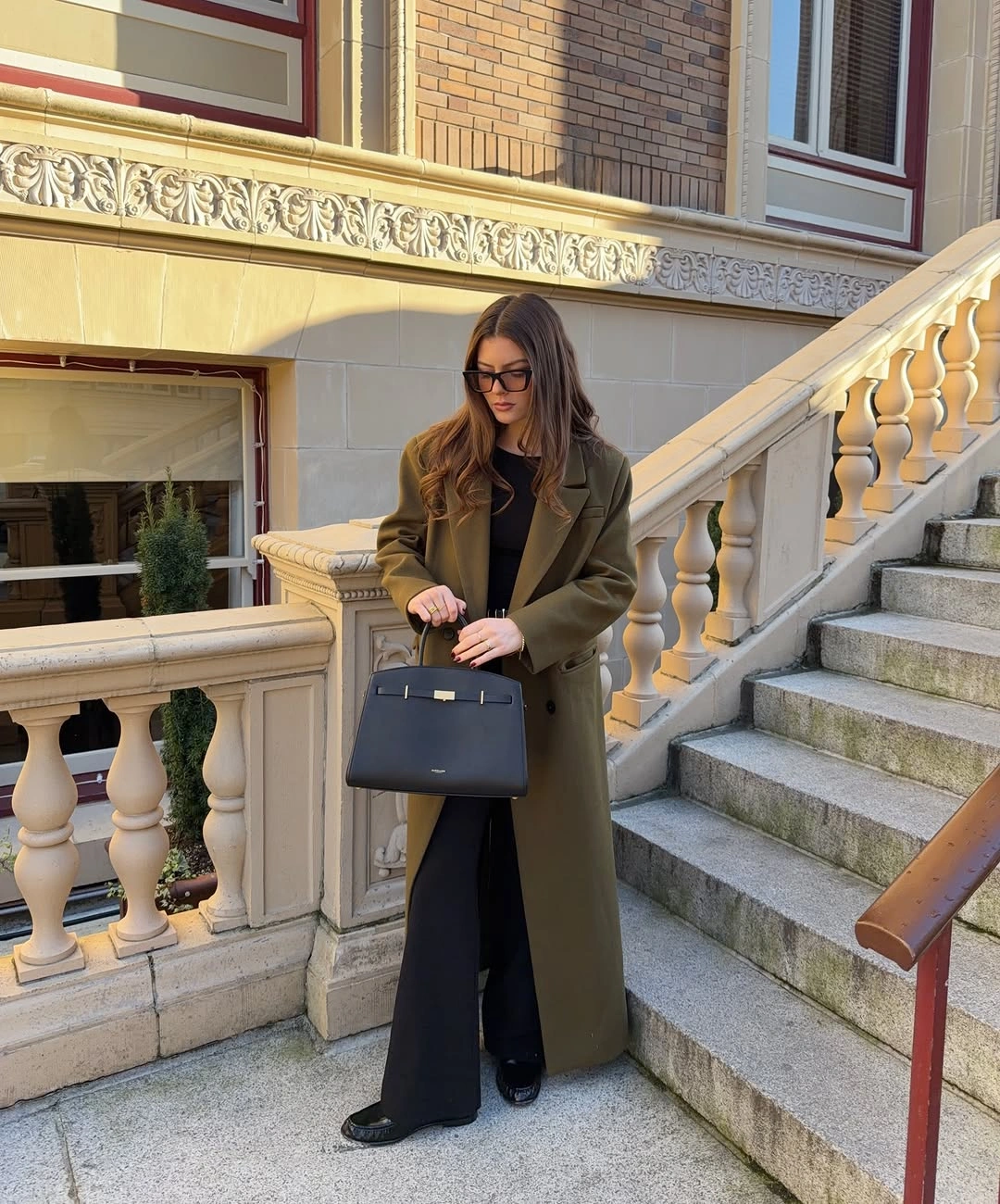 Olive long coat over black top and very wide trousers