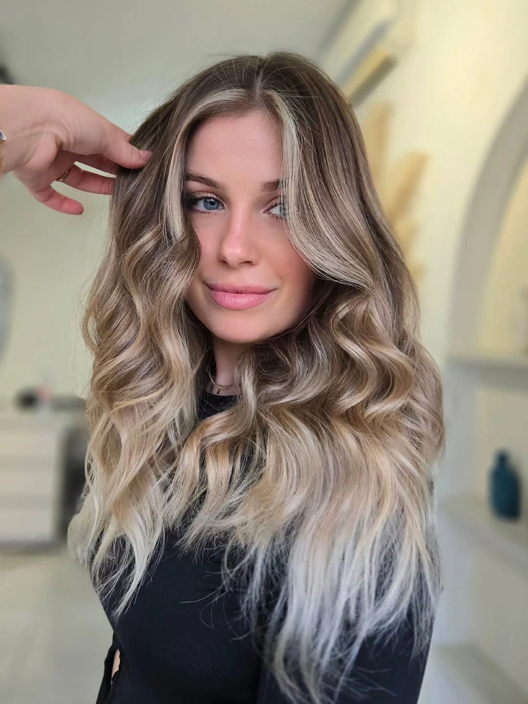 Rooted beige blonde waves with pale face framing sections