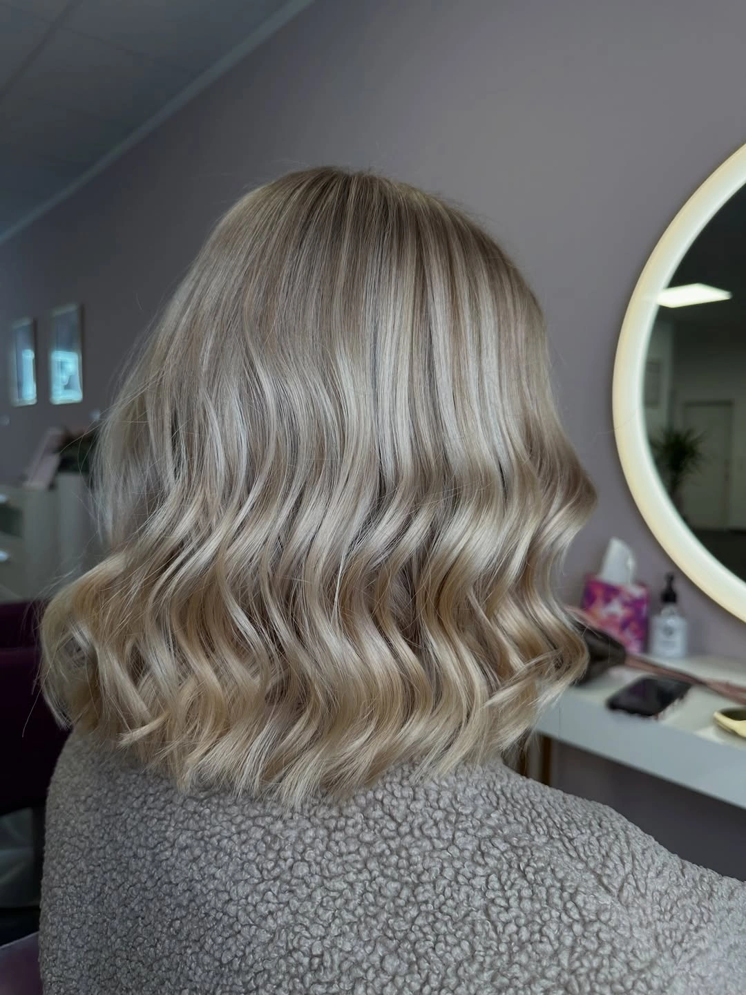 Short wavy icy beige blonde lob with darker roots