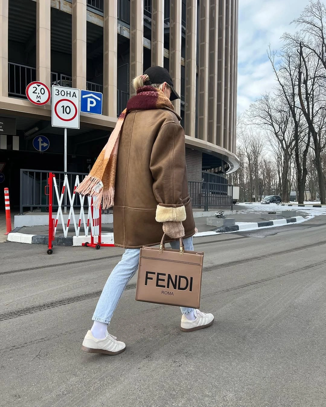 Brown shearling-looking coat with scarf, light jeans, and white sneakers
