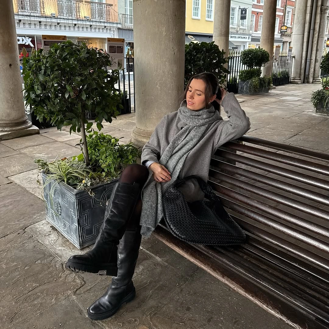 Oversized gray knit-looking layer, long scarf, tights, and tall black boots