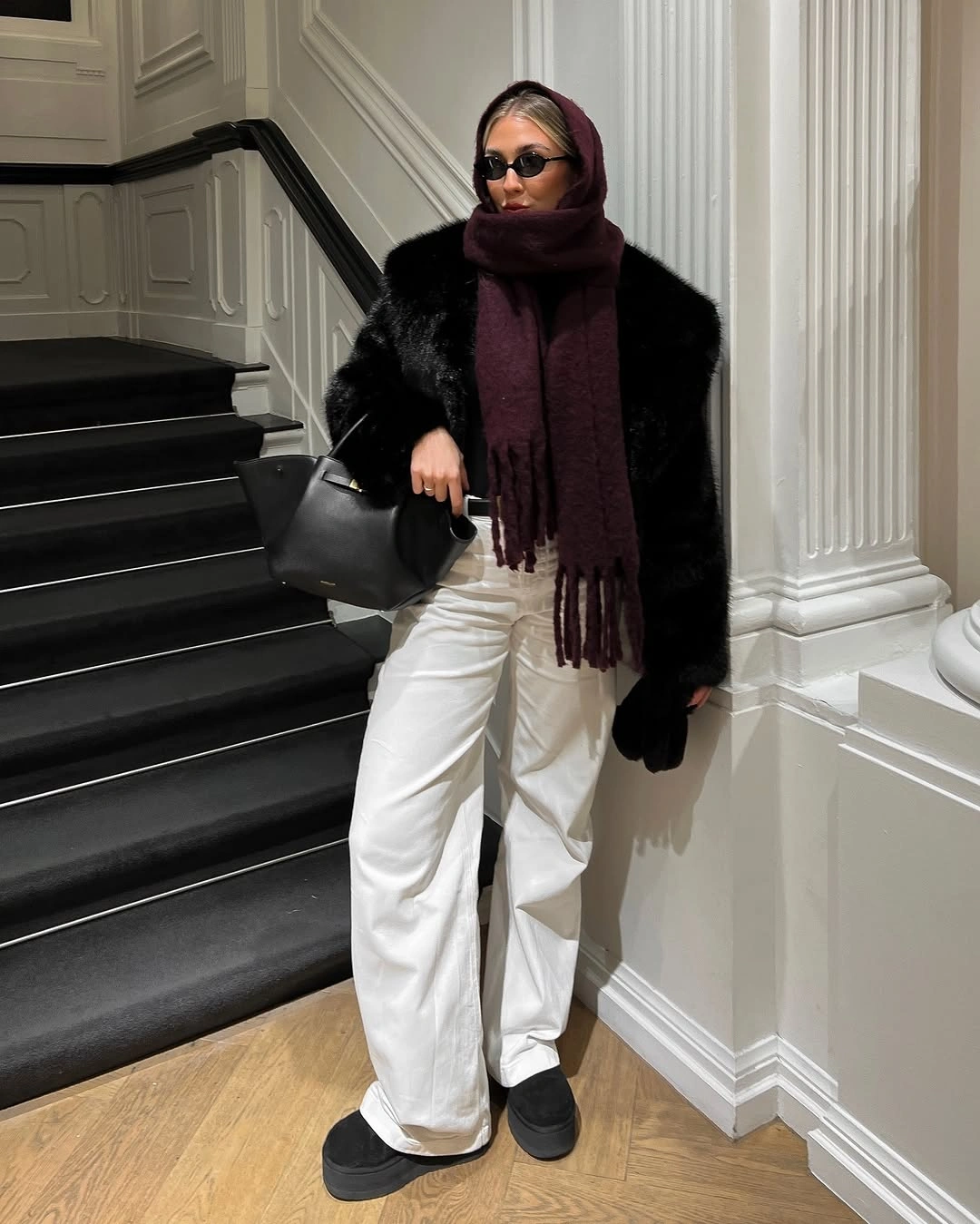 Black plush-looking coat, burgundy scarf, white trousers, and platform shoes
