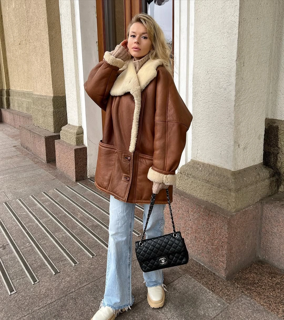 Brown oversized coat with light jeans, pale boots, and black bag