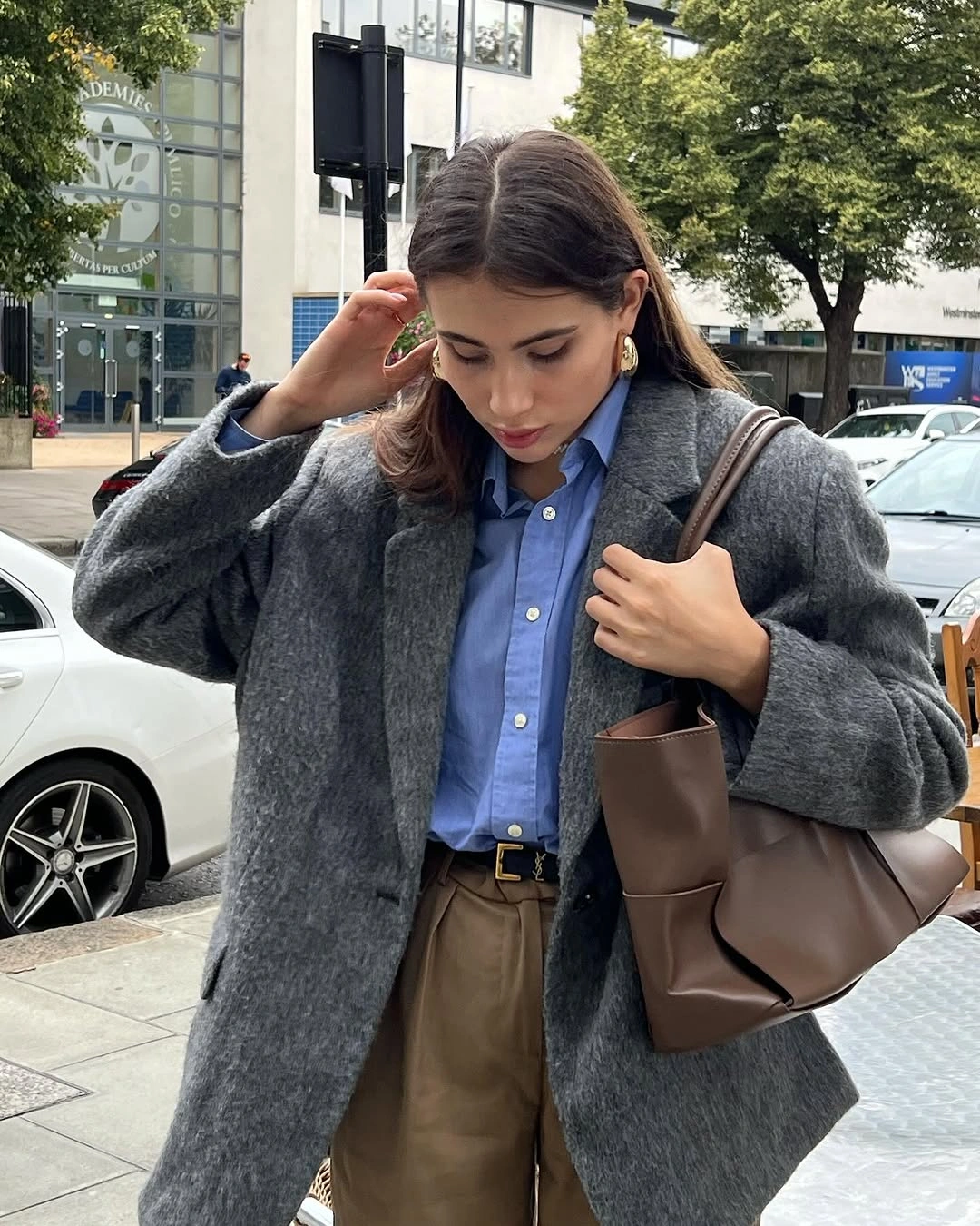 Charcoal-gray coat over blue shirt, brown trousers, and brown tote