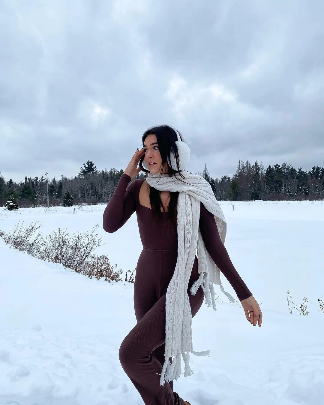 Burgundy fitted outfit with long white scarf and white earmuffs in snow