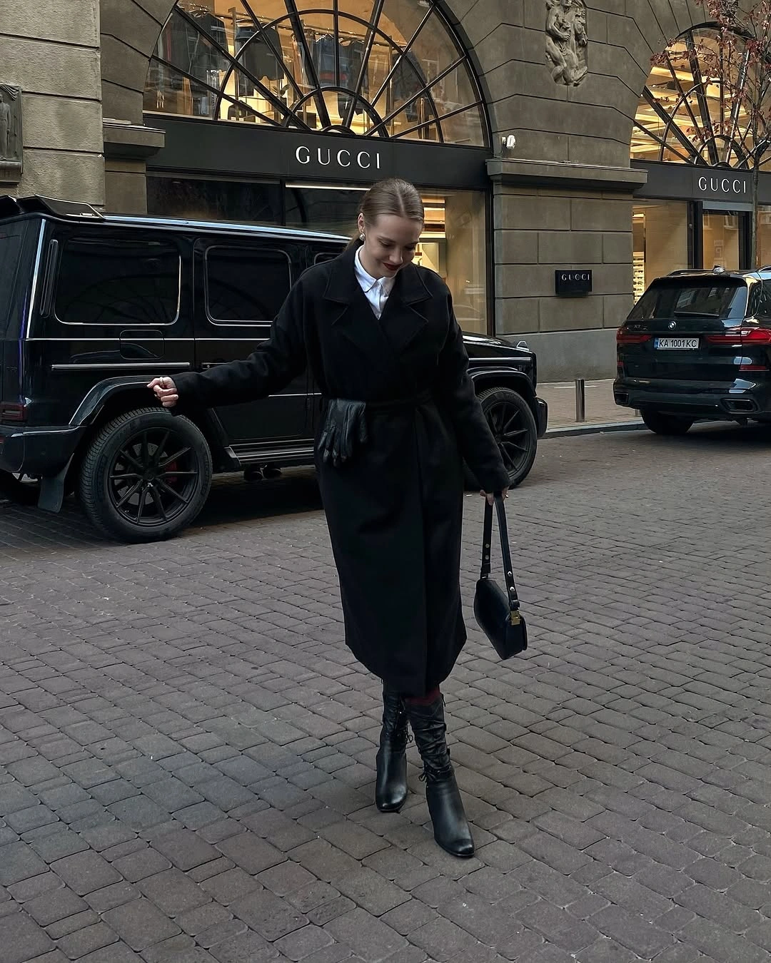 Long belted black coat with white collar, gloves, boots, and bag