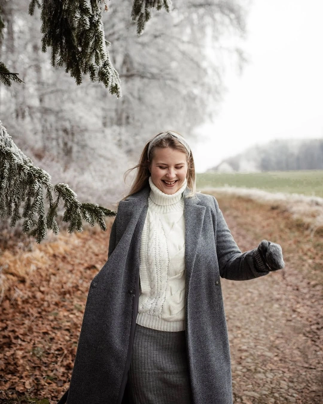 Woman in long gray coat, ivory turtleneck sweater, and gloves
