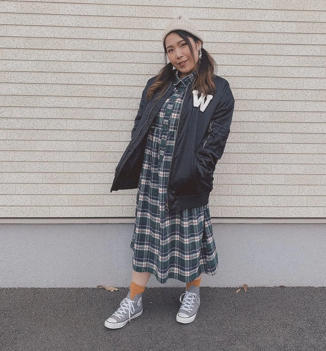 Person in dark bomber jacket, plaid dress, sneakers, and beanie