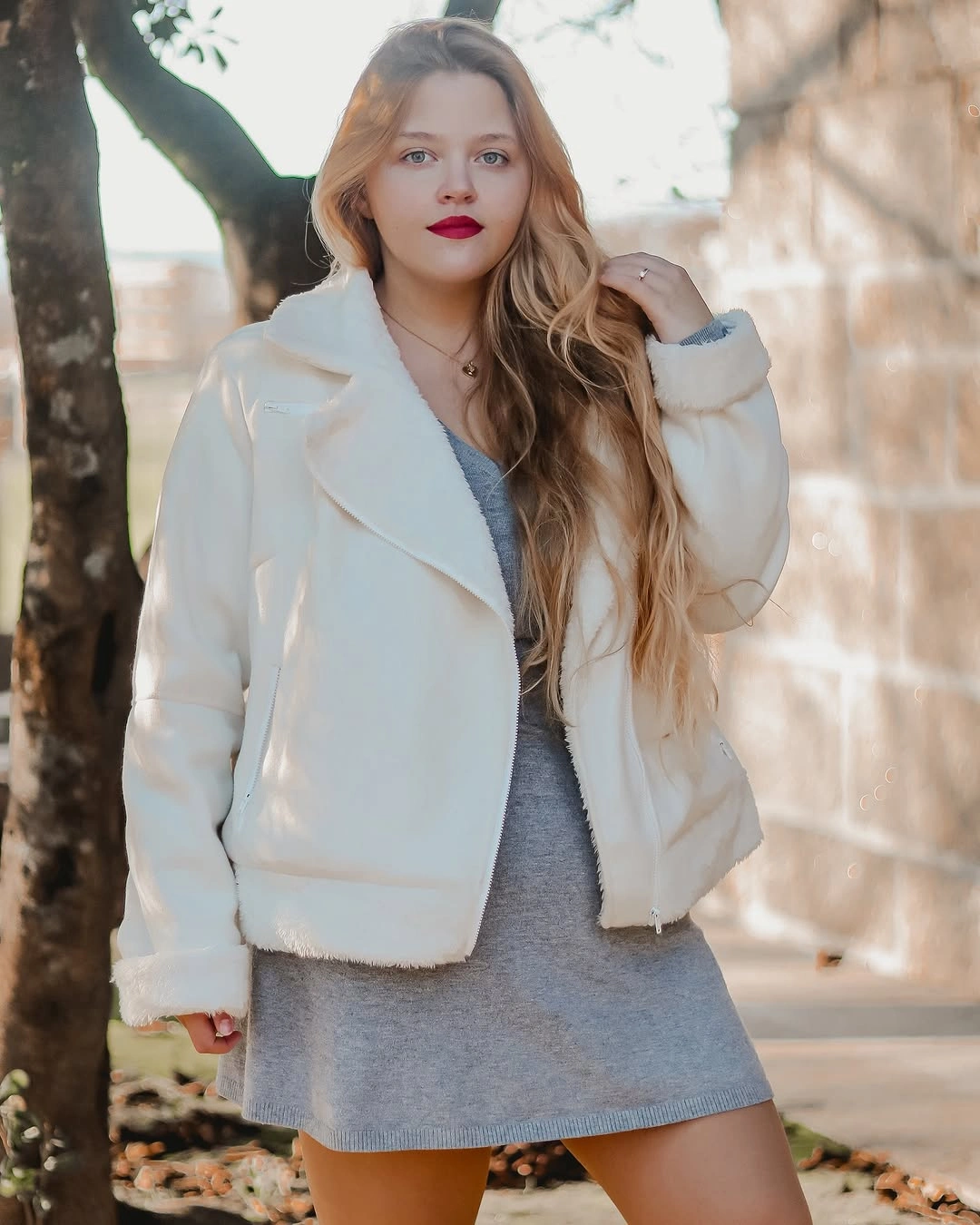 Woman in cream jacket, gray short dress, and red lipstick