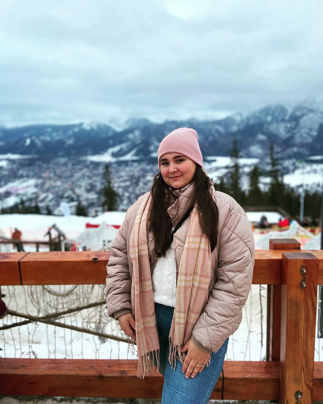 Woman in pale quilted jacket, pink beanie, scarf, and jeans