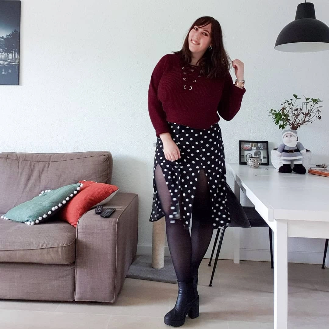 Woman in burgundy sweater, polka-dot skirt, tights, and black boots