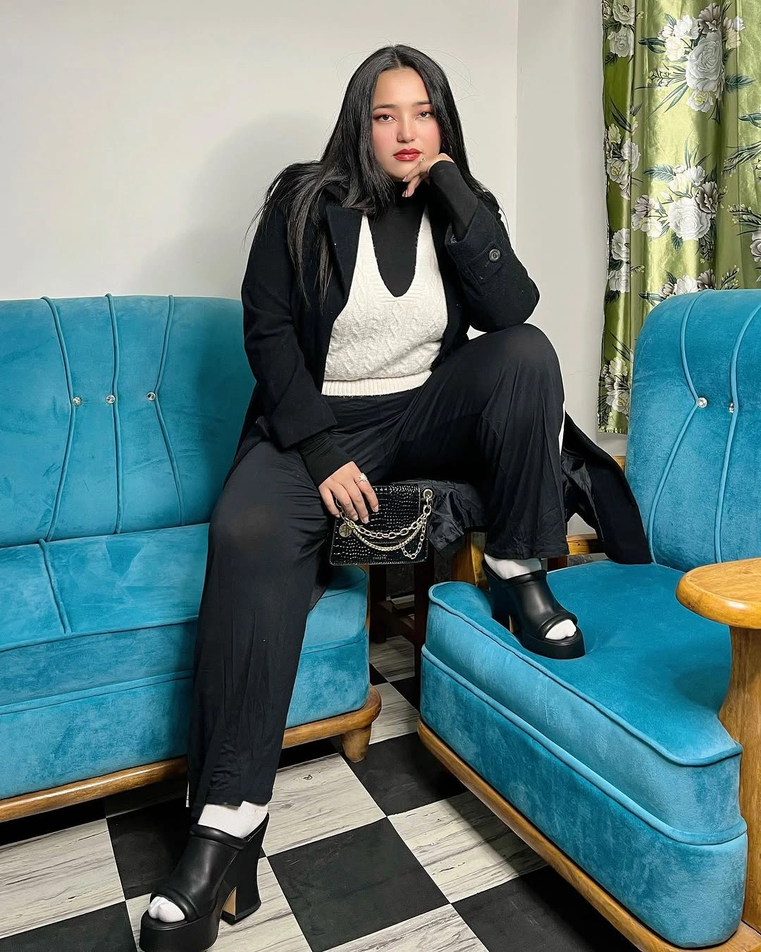 Seated woman in black layers, cream vest, white socks, and platforms