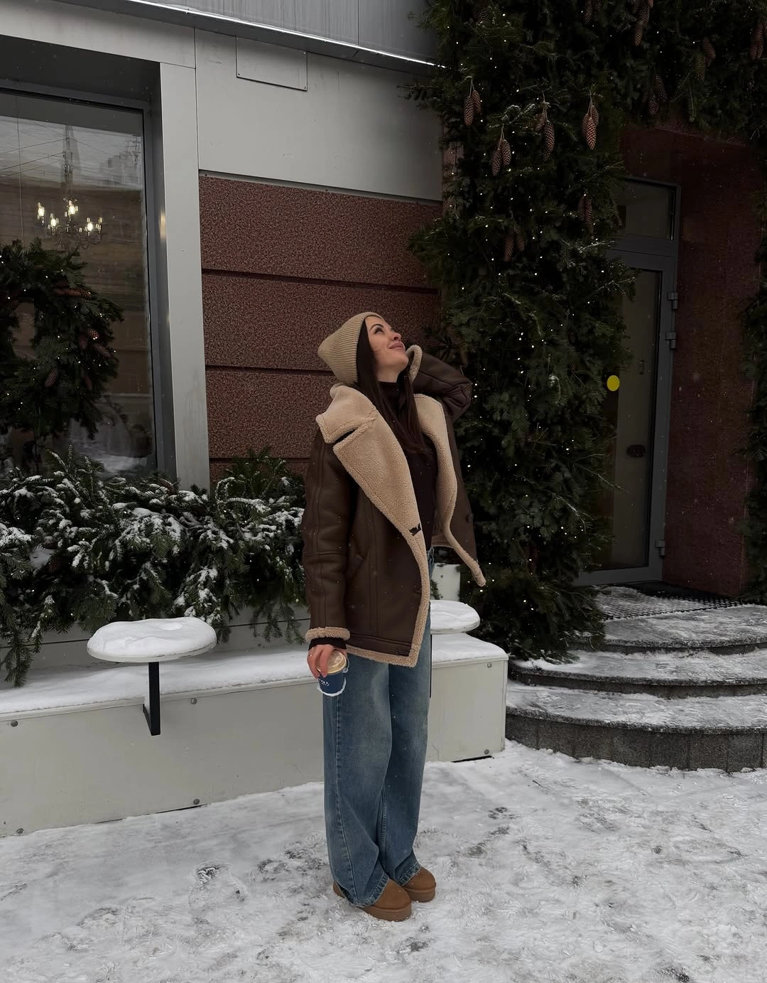 Brown jacket with pale trim, wide jeans, beanie, and tan shoes