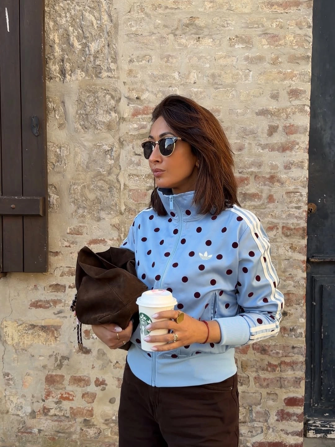 Powder-blue dotted top with brown trousers, sunglasses, bag, and cup