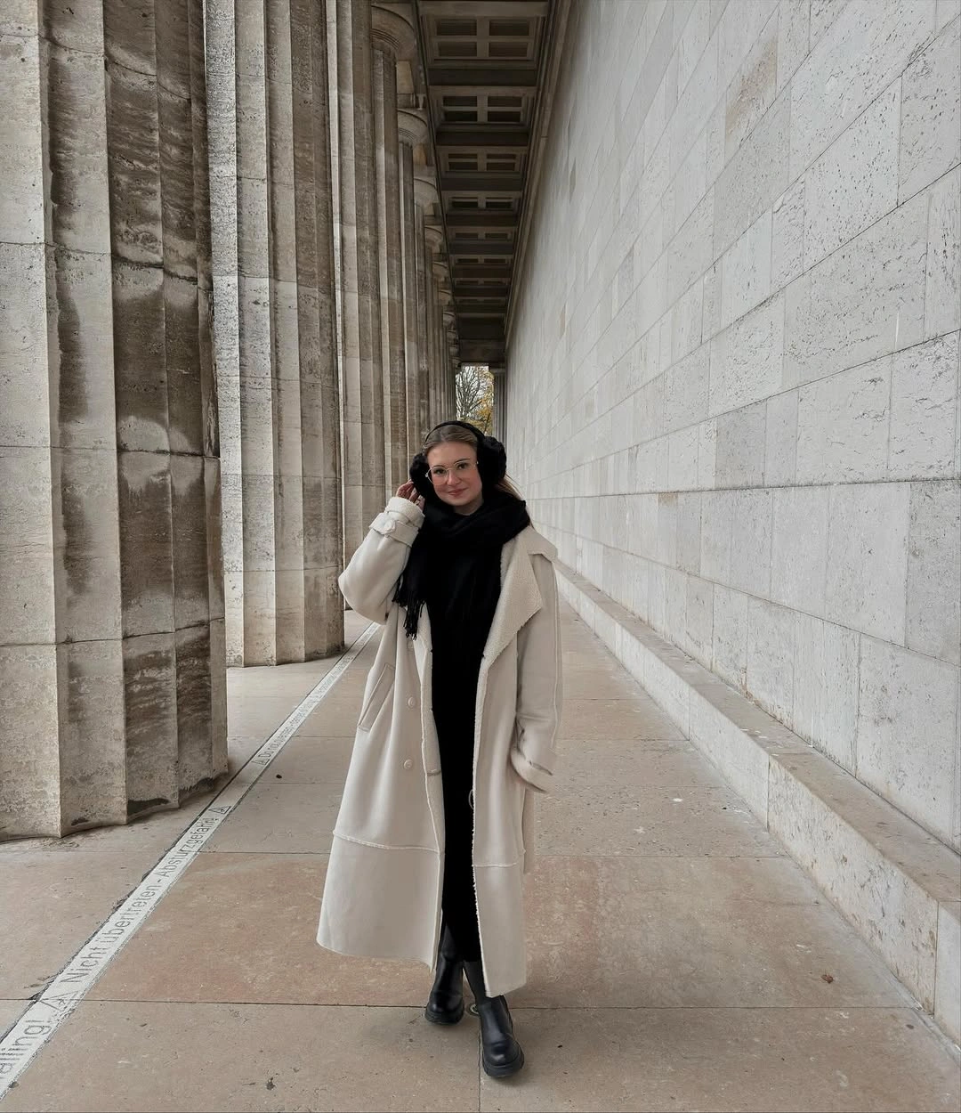 Long off-white coat with black scarf, trousers, earmuffs, and boots