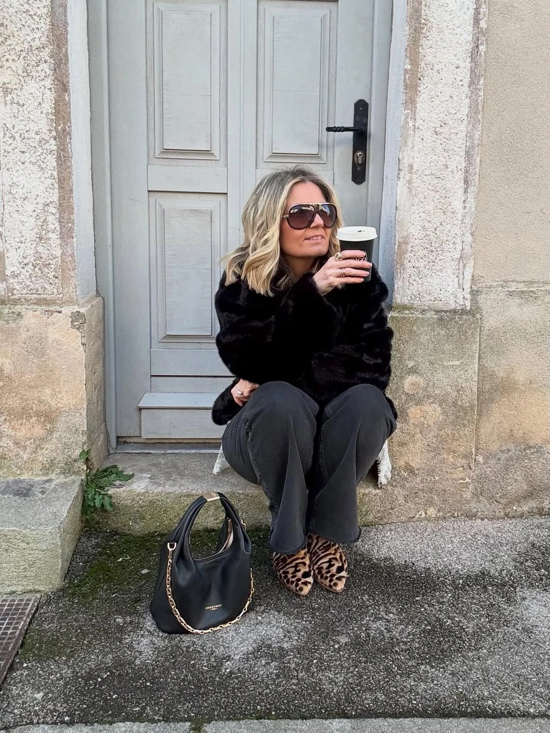 Black plush jacket, charcoal trousers, leopard shoes, sunglasses, and rounded handbag