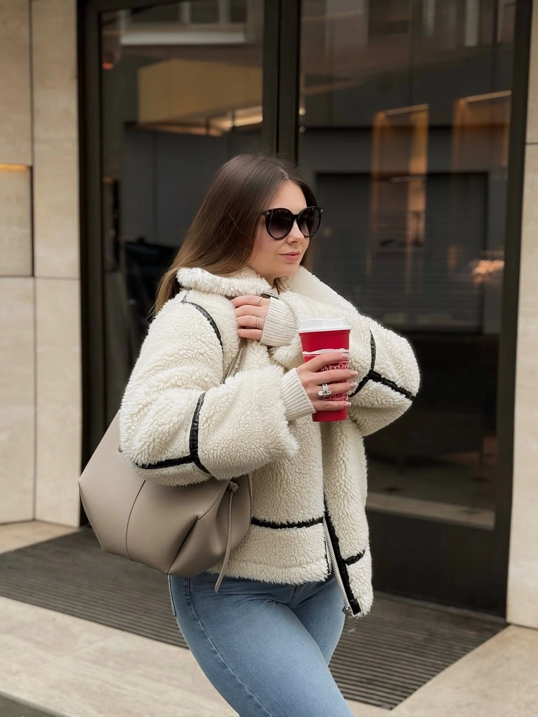 Cream textured jacket with black piping, blue jeans, and taupe tote