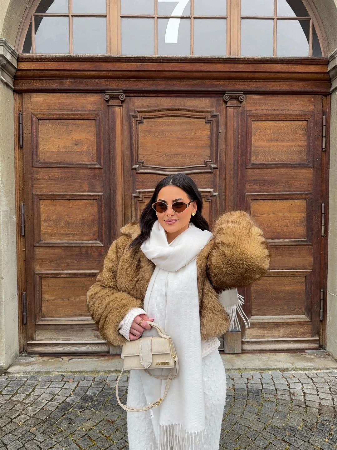 Golden-brown plush jacket, long white scarf, sunglasses, and pale handbag