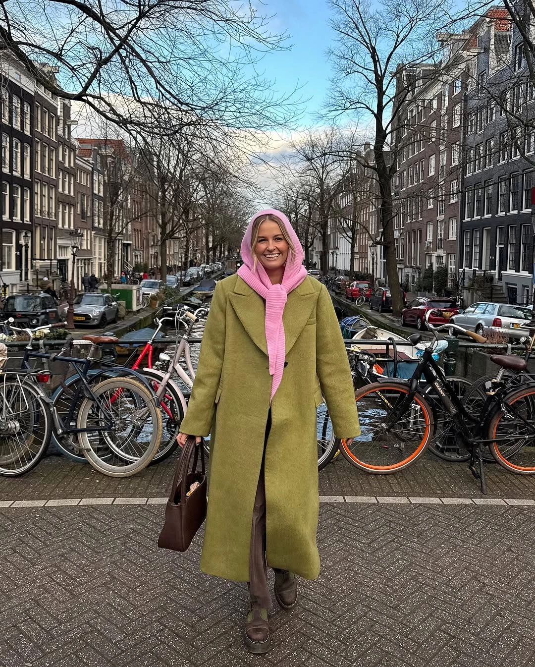Olive long coat over pink hoodie with brown boots and dark handbag