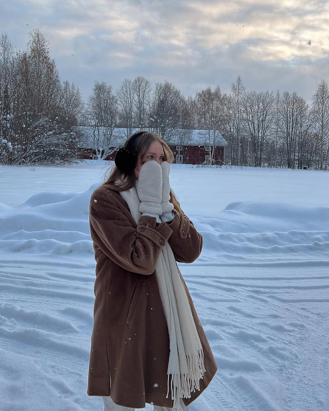 Long brown coat with cream scarf mittens and dark trousers in snow
