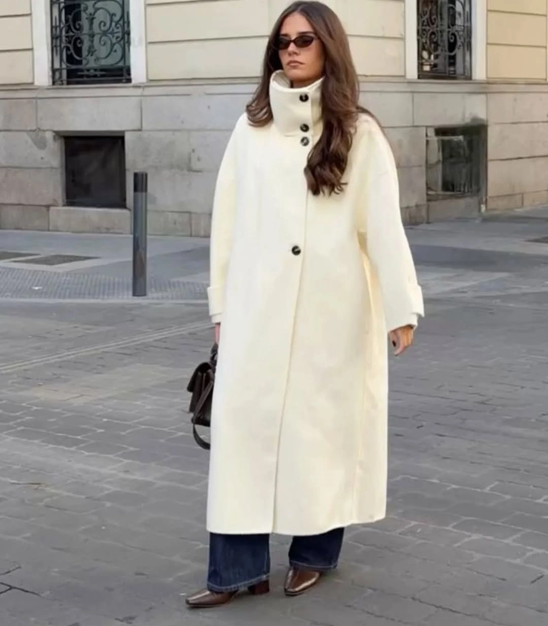 Ivory buttoned long coat with blue jeans brown pointed shoes and dark bag