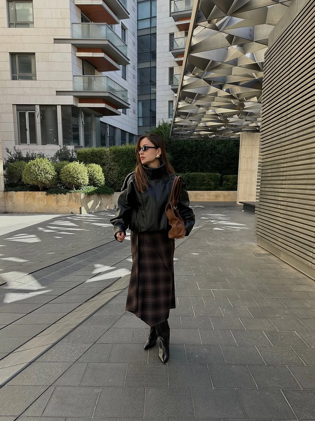 Black leather-look jacket with dark plaid midi skirt and ankle boots